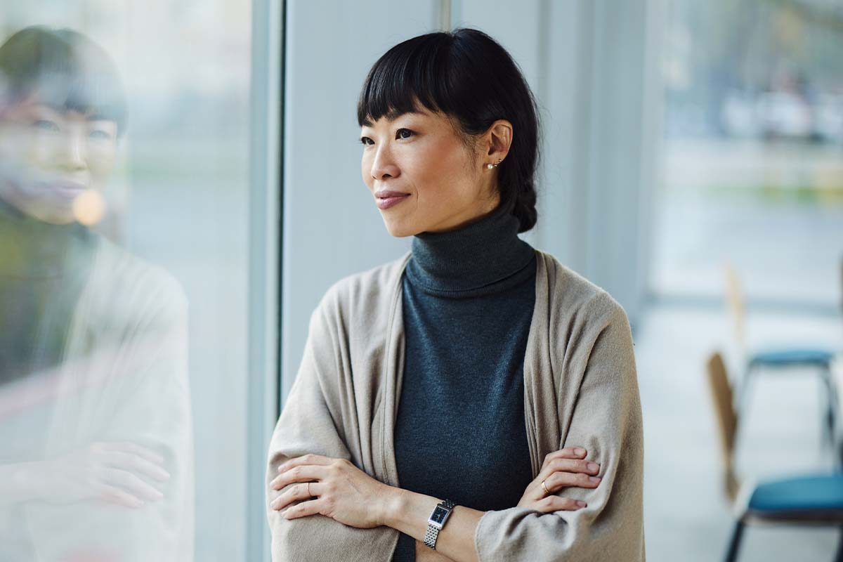 a woman in a conference room looking out a window while crossing her arms after getting clearer vision with lens replacement surgery in Bend, OR